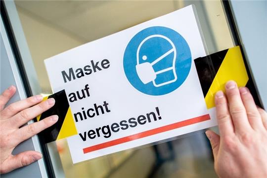 Ein Hausmeister einer Schule klebt ein Schild zur Maskenpflicht auf. Foto: Hauke-Christian Dittrich/dpa