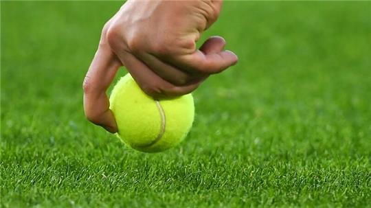 Ein Helfer sammelt einen Tennisball vom Spielfeld in der Volkswagen Arena auf.