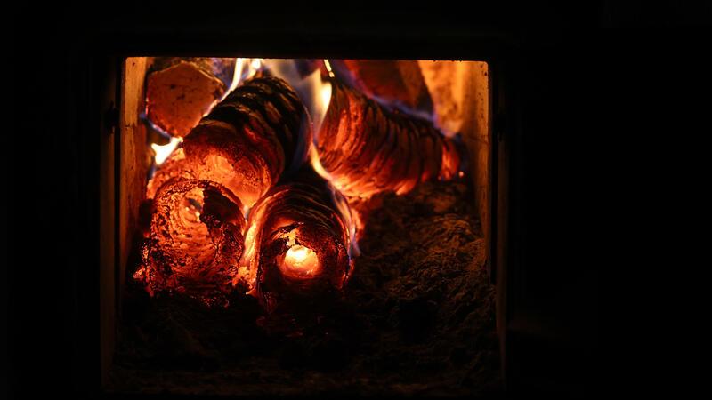 Ein Holzofen wird vom Hausflur aus mit Holzbriketts geheizt.