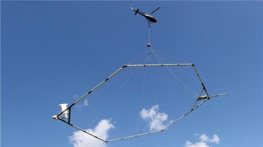 Ein Hubschrauber schleppt eine Antenne über den Grund, die den Aufbau des Untergrundes misst.