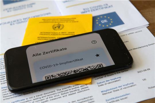 Ein Impfpass und ein Smartphone, auf dem die App CovPass läuft.