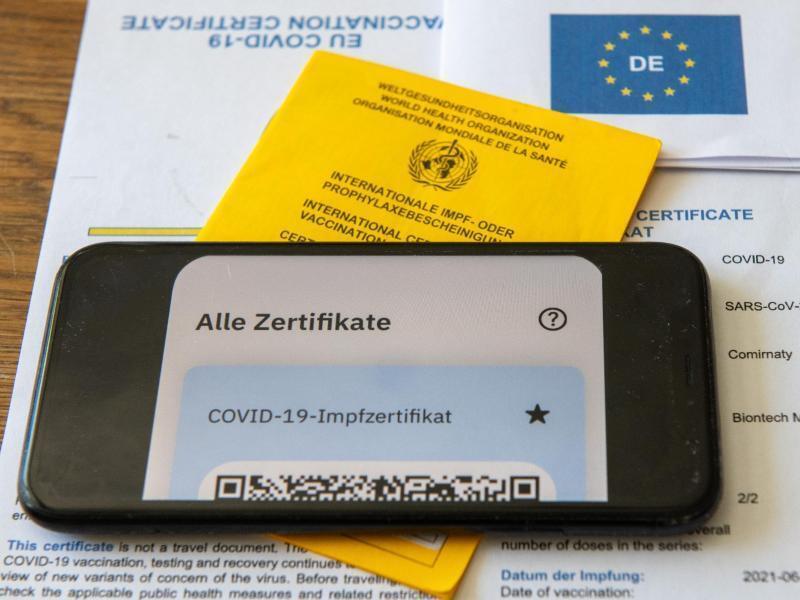 Ein Impfpass und ein Smartphone, auf dem die App CovPass läuft, liegen auf einem Impfzertifikat. Foto: Stefan Puchner/dpa