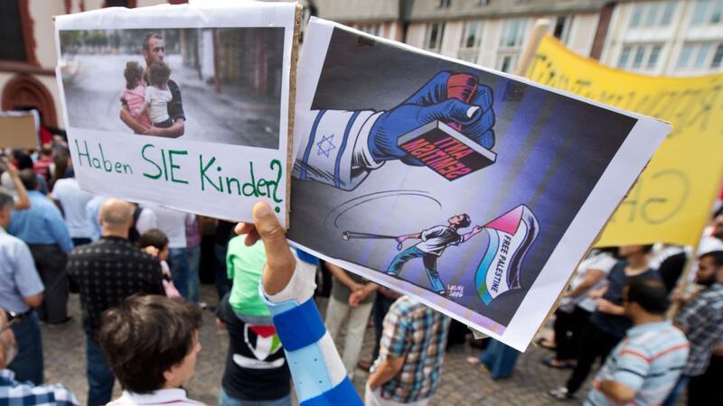 Ein Junge hält ein Plakat hoch, auf dem ein propalästinensischer Demonstrant unter einem Stempel mit der Aufschrift  „Anti Semitismus“ steht.