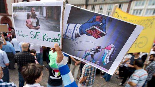 Ein Junge hält ein Plakat hoch, auf dem ein propalästinensischer Demonstrant unter einem Stempel mit der Aufschrift  „Anti Semitismus“ steht.