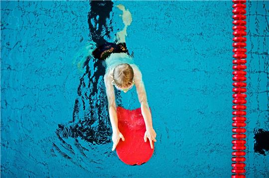 Ein Junge lernt mit einer Schwimmhilfe die Technik. Symbolfoto: dpa/Vennenbernd