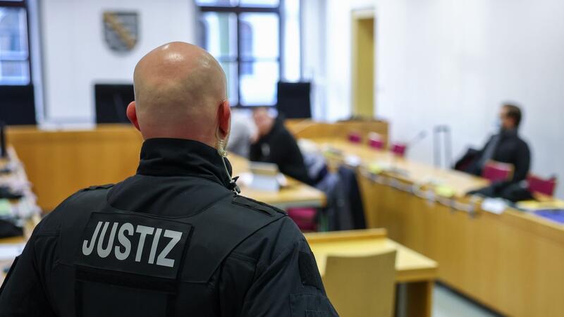 Ein Justizbeamter steht vor Prozessbeginn vor einigen Angeklagten im Landgericht Chemnitz.