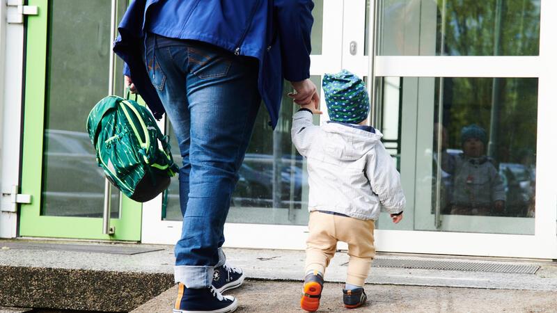 Buxtehude kürzt Kita-Zeiten – Erstmals Einschränkungen in Ferien Ein Kind geht mit seiner Mutter zum Eingang einer Kita. Erwerbstätige Eltern müssen sich in Buxtehude auf kürzere Betreuungszeiten einstellen.