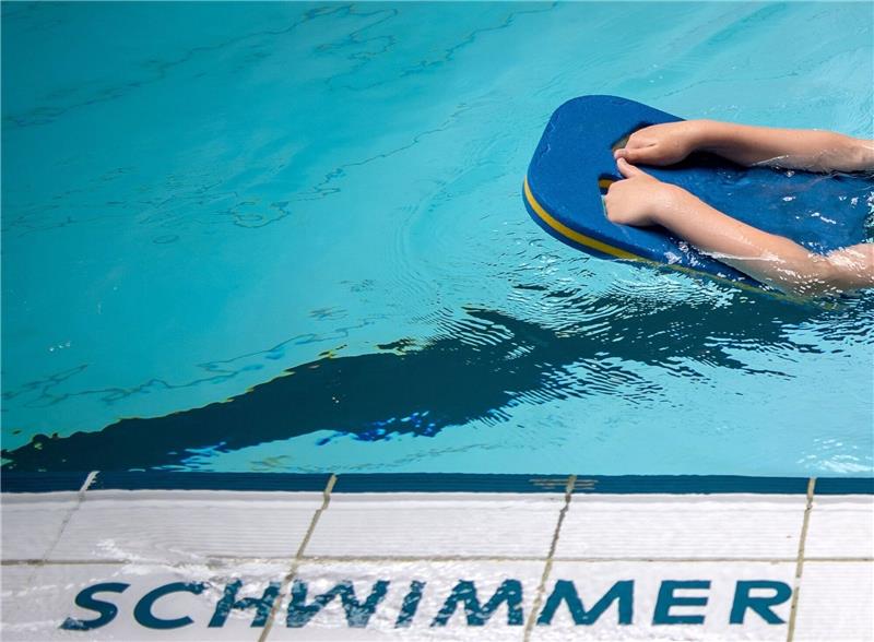 Ein Kind schwimmt mit Brett in einem Schwimmbecken.