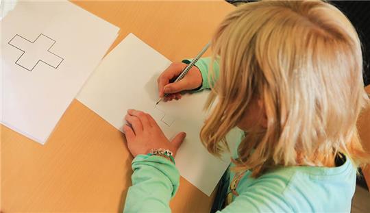 Ein Kind zeichnet ein auf einem Zettel abgebildetes Kreuz ab. Im Rahmen der Schuleingangsuntersuchungen stellt das Kreis-Gesundheitsamt fest, ob ein Kind bereit für die Schule ist. Foto: picture alliance/dpa