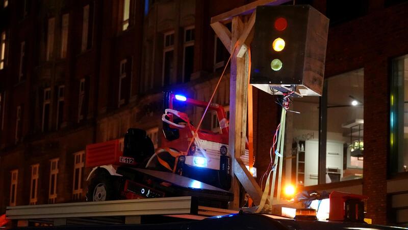 Ein Kleinlaster hat einen Holzgalgen aufs Dach geschnallt, an dem eine Ampel befestigt ist.