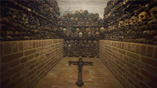 Ein Kreuz liegt vor den gestapelten Totenschädeln.