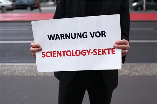 Ein Mann demonstriert am Potsdamer Platz am Rande einer Veranstaltung der Scientology-Sekte mit einem Schild gegen die Organisation.