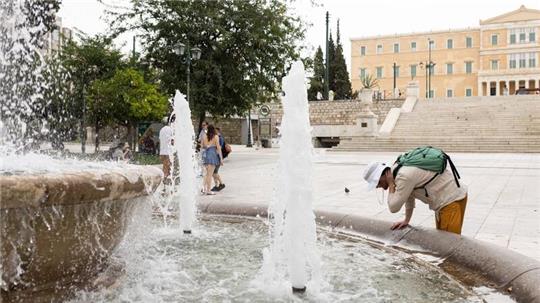 Ein Mann erfrischt sich an einem  Springbrunnen auf dem Athener Syntagma-Platz.