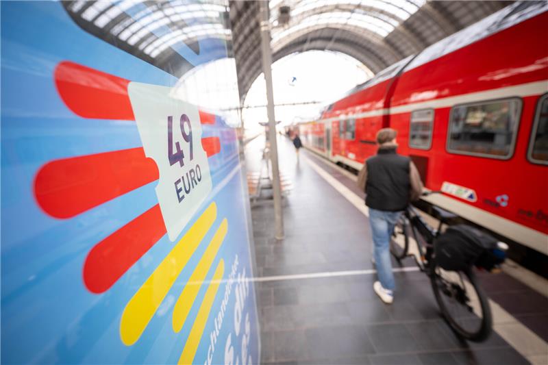 Deutschlandticket hat Startprobleme Ein Mann geht am Hauptbahnhof mit seinem Fahrrad zwischen der Werbung für das Deutschlandticket und einer Regionalbahn vorbei. Seit Montag gilt bundesweit das 49 Euro teure Deutschlandticket im öffentlichen Personennahverkehr. Foto: Sebastian Gollnow/dpa
