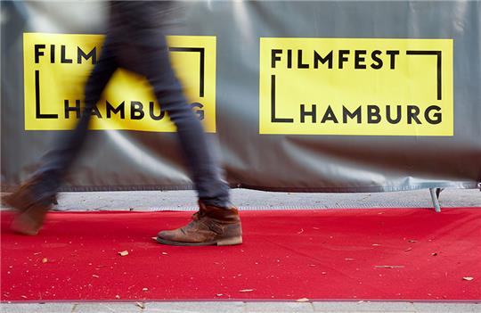 Ein Mann geht auf dem roten Teppich am Logo mit der Aufschrift «Filmfest Hamburg» vorbei. Foto: Georg Wendt/dpa