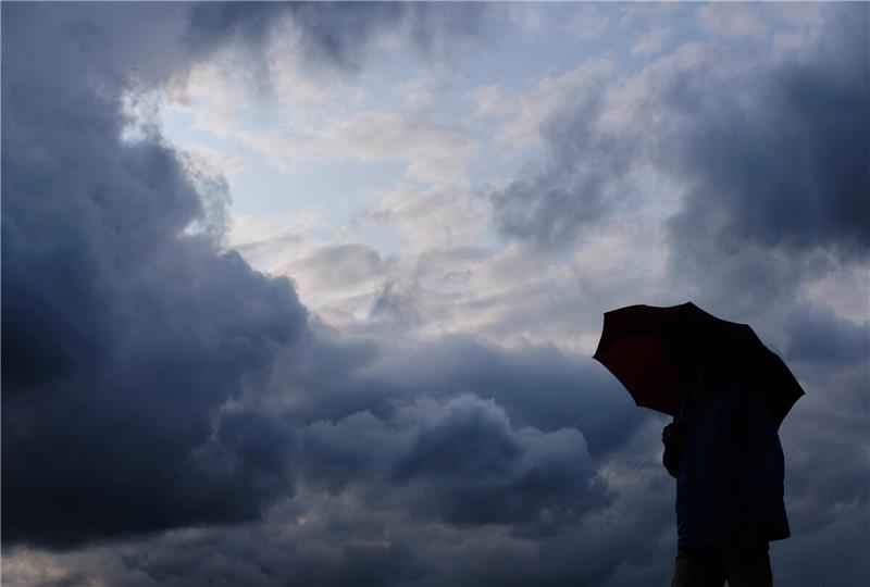 Ein Mann geht mit einem Regenschirm vor aufziehenden dunklen Wolken spazieren.Das Wetter könnte für die Menschen im Kreis Stade ab Mittwochmittag sehr ungemütlich werden. Foto: Martin Gerten/dpa
