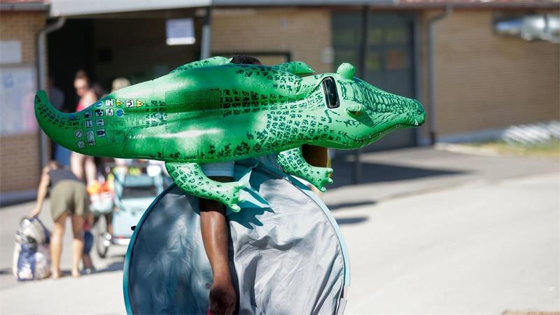 Ein Mann geht mit einem grünen Schwimm-Krokodil in ein Schwimmbad in Baden-Württemberg.