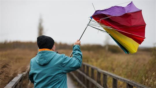 Ein Mann hält auf dem Steg am Federsee seinen Regenschirm fest, der von einer Sturmböe erfasst wird.