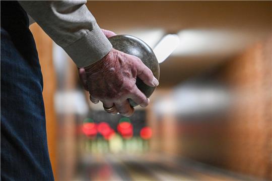 Ein Mann hält auf der Kegelbahn eine Kugel in den Händen (Symbolbild). Foto: Jens Kalaene/dpa
