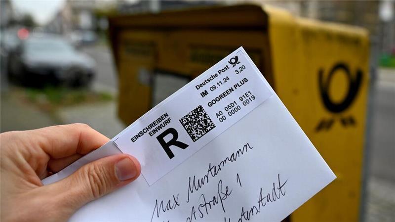 Ein Mann hält ein sogenanntes Einwurf-Einschreiben vor einen Briefkasten (gestellte Szene).