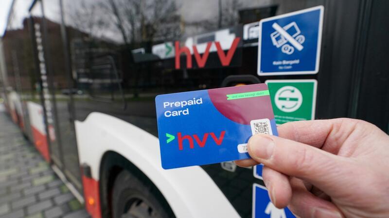 Ein Mann hält eine Prepaid Card zum bargeldlosen Ticketkauf vor einem Linienbus des Hamburger Verkehrsverbunds (HVV) hoch.