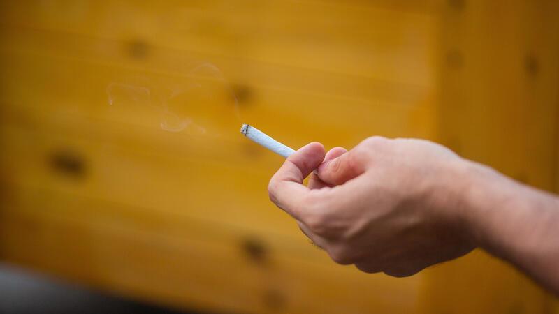 Ciao, Zigarette! Helfen Nikotinpflaster beim Rauchstopp? Ein Mann hält eine brennende Zigarette in der Hand, während er raucht.
