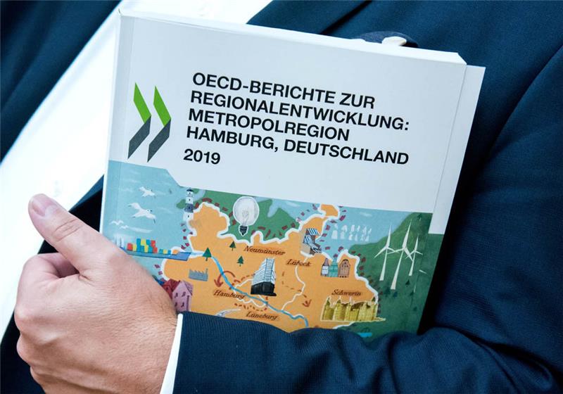 Ein Mann hält einen OECD-Bericht zur Entwicklung der Metropolregion Hamburg in seinem Arm. Foto: Daniel Bockwoldt/dpa