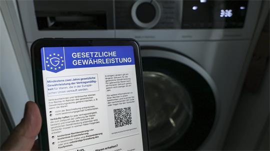 Ein Mann informiert sich vor einer Waschmaschine über die neuen EU-Label zu Gewährleistung und Garantie. 