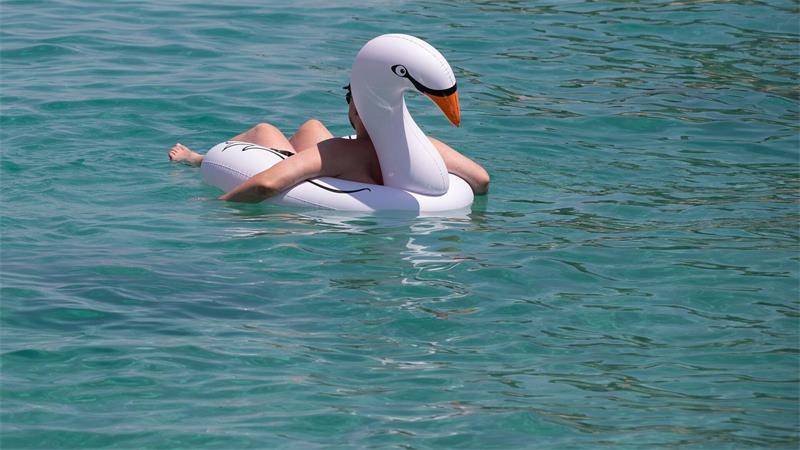 Ein Mann lässt sich auf einem Schwimmtier am Strand von Cala Vinyes auf Mallorca im türkisblauen Wasser treiben.