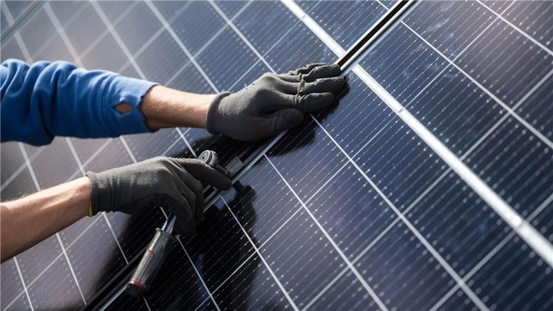 Ein Mann montiert Photovoltaikmodule auf dem Dach eines Hauses.