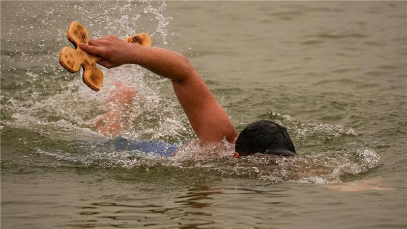 Ein Mann schwimmt mit einem von drei Holzkreuzen, die der orthodoxe Erzbischof Teodosie bei Harsova in die Donau geworfen hat, damit die Menschen sie zurückholen können, während eines Gottesdienstes einen Tag vor dem Dreikönigsfest.