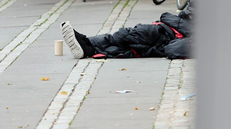 Mehr Wohnungslose suchen 2023 Hilfe bei Diakonie Ein Mann sitzt in einen Schlafsack gehüllt auf dem Asphalt in der Innenstadt.