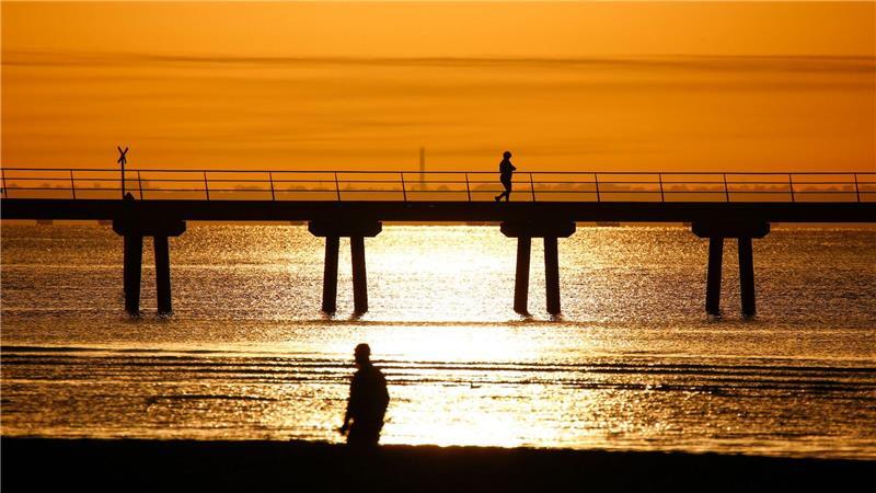 Ein Mann spaziert bei Sonnenaufgang am Altona Pier entlang.