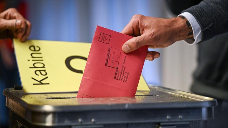 Wahlhelferin mit Kopftuch rassistisch beleidigt Ein Mann steckt seine Stimmzettel in einem Briefumschlag in die Wahlurne.