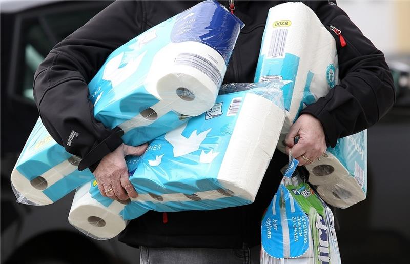 Ein Mann trägt eingekauftes Toilettenpapier und Küchenrollen aus einem Supermarkt. Foto: Rene Traut/dpa