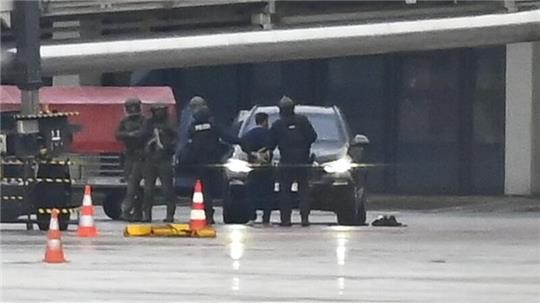 Ein Mann wird auf dem Flughafen von der Polizei weggeführt.