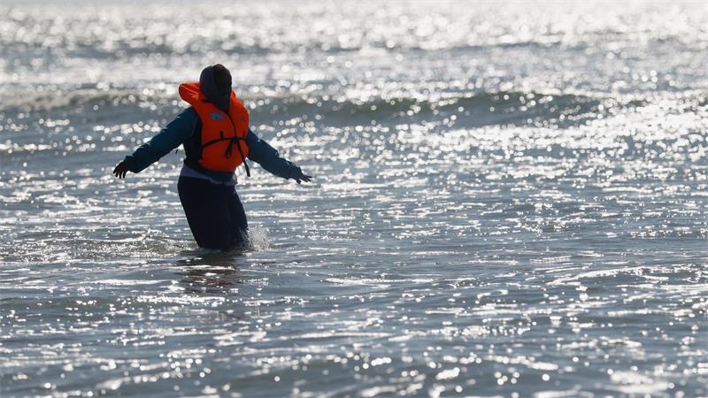 Ein Migrant läuft in Nordfrankreich im Meer nahe der Küste, während er versucht, den Ärmelkanal mit einem Schlauchboot von Frankreich nach Großbritannien zu überqueren.
