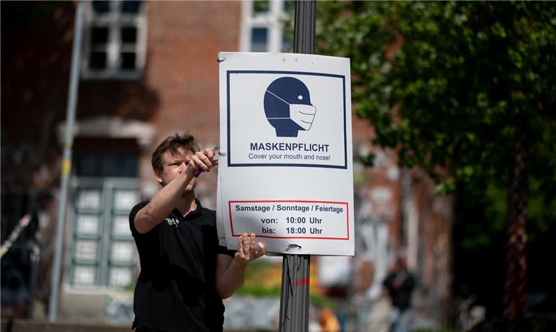 Ein Mitarbeiter der Firma Scharlau hängt in Hamburg ein Hinweisschild zur Maskenpflicht auf St. Pauli ab. Foto: Daniel Reinhardt/dpa