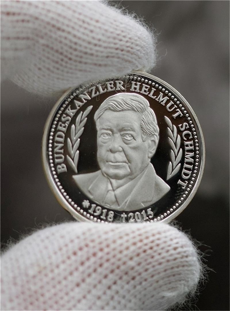 Ein Mitarbeiter der Hambur- gischen Münze zeigt eine Gedenkmünze mit dem Porträt des früheren Bundeskanzlers Helmut Schmidt. Heimken/dpa