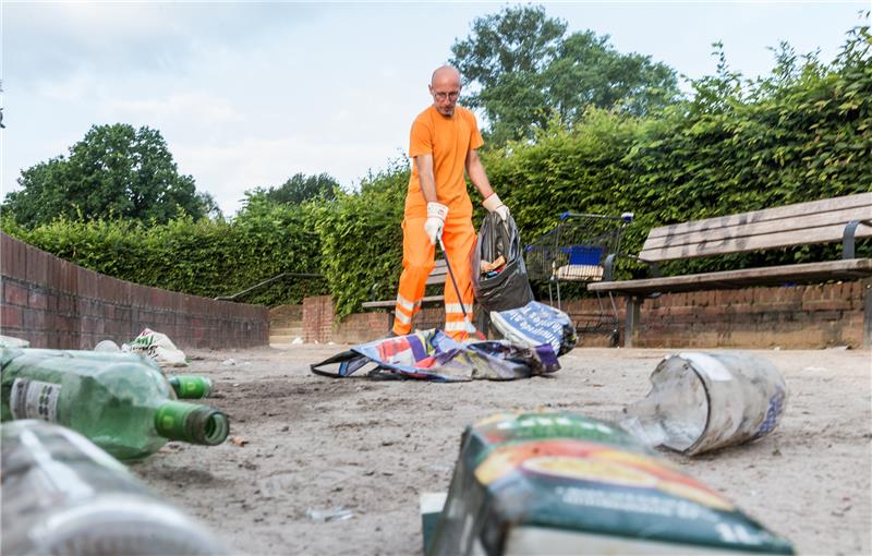 Ein Mitarbeiter der Stadtreinigung entfernt am frühen Morgen den Müll im Stadtpark, der dort nach einer lauen Sommernacht zurückgelassen wurde. Foto: Markus Scholz/dpa