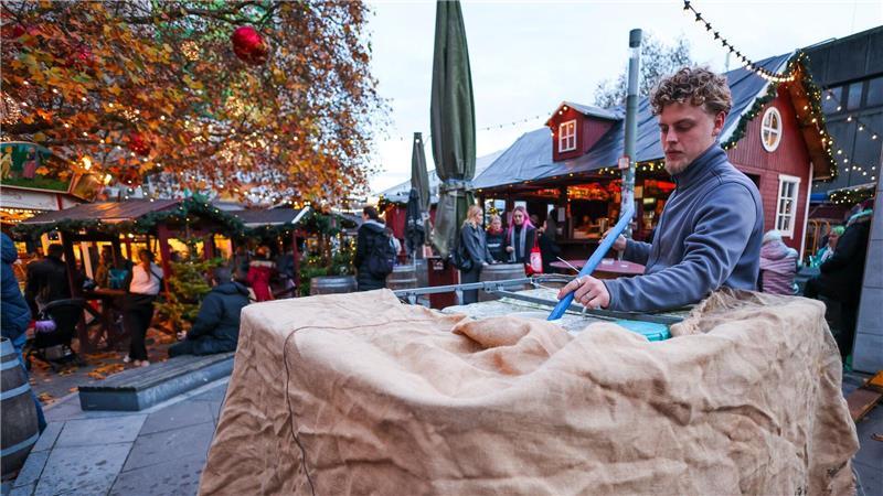 Ein Mitarbeiter eines kleinen Weihnachtsmarkts befüllt einen Kunststofftank mit Wasser und verkleidet ihn mit Stoff.