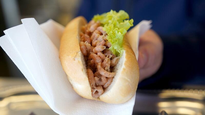 Schleswig-Holsteins Ostseeküste feiert Weltfischbrötchentag Ein Mitarbeiter reicht einem Kunden ein Brötchen mit Nordseekrabben über den Tresen eines Fischbrötchen-Imbisses.