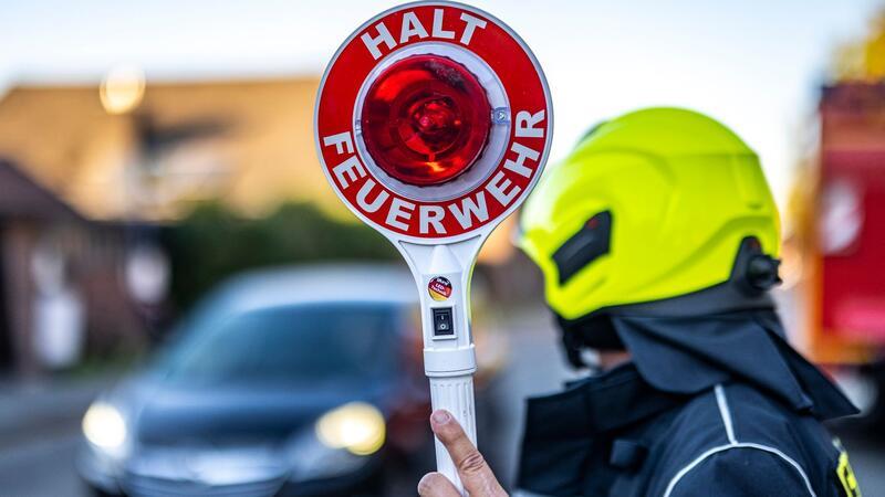Ein Mitglied der Feuerwehr hält eine Kelle mit der Aufschrift „Halt Feuerwehr“ in die Höhe.