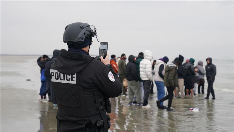 Ein Mitglied der französischen Behörden filmt eine Gruppe von Menschen, bei denen es sich vermutlich um Migranten handelt, die am Strand von Gravelines, Frankreich, warten, während sie versuchen, ein kleines Boot zu besteigen, um den Ärmelkanal zu überqueren.