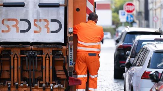 Ein Müllmann steht auf einem Müllfahrzeug.
