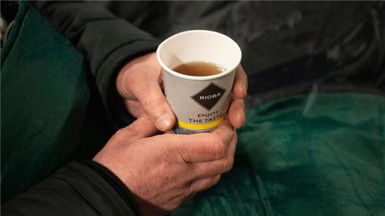 Ein Obdachloser hält einen Becher Tee in der Hand.