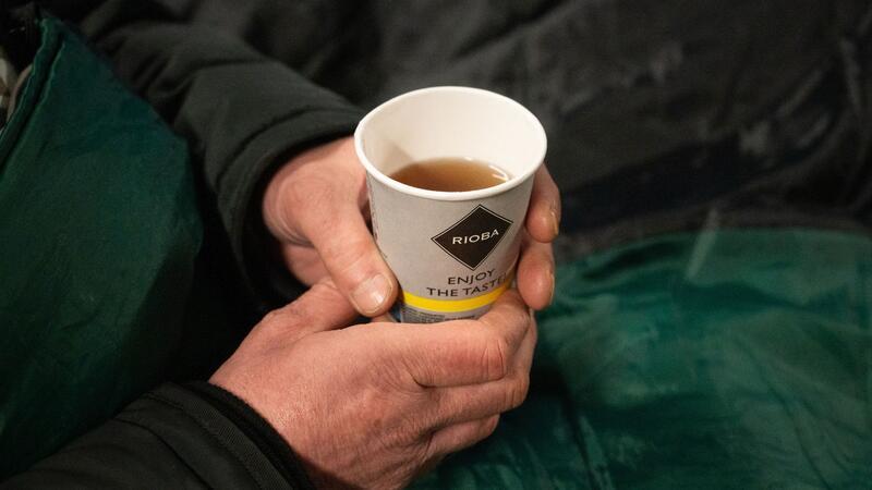 Container zum Schutz von Obdachlosen aufgestellt Ein Obdachloser hält einen Becher Tee in der Hand.