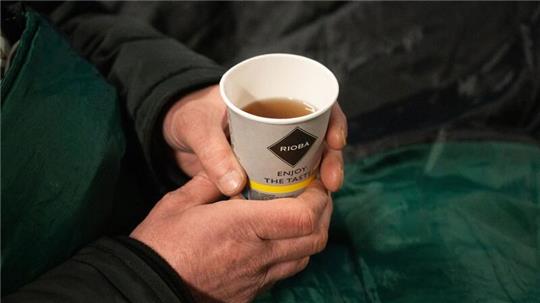 Ein Obdachloser hält einen Becher Tee in der Hand.