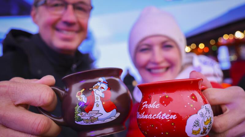 In Hamburg ist hier die Weihnachtsmarkt-Saison eröffnet Ein Paar hält zwei Tassen mit heißem Glühwein kurz nach der Eröffnung des Santa Pauli Weihnachtsmarkts auf dem Spielbudenplatz.