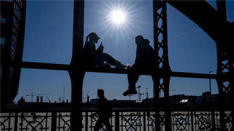 Ein Pärchen sitzt in der Sonne auf dem Geländer der Hackerbrücke in München. 